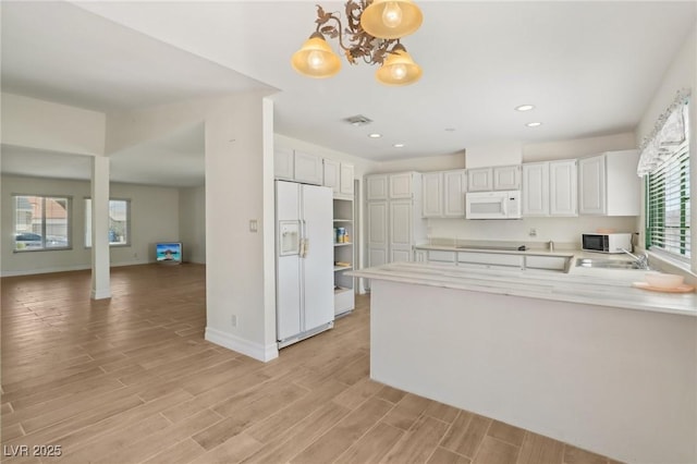 kitchen with a peninsula, light countertops, white appliances, and light wood-style flooring