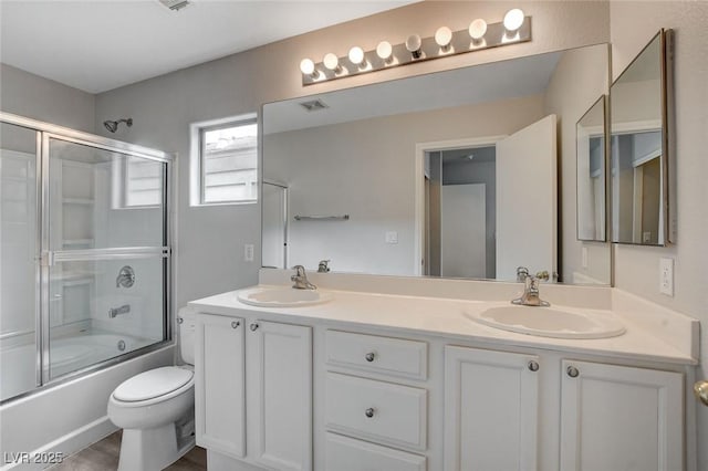 bathroom featuring a sink, bath / shower combo with glass door, double vanity, and visible vents