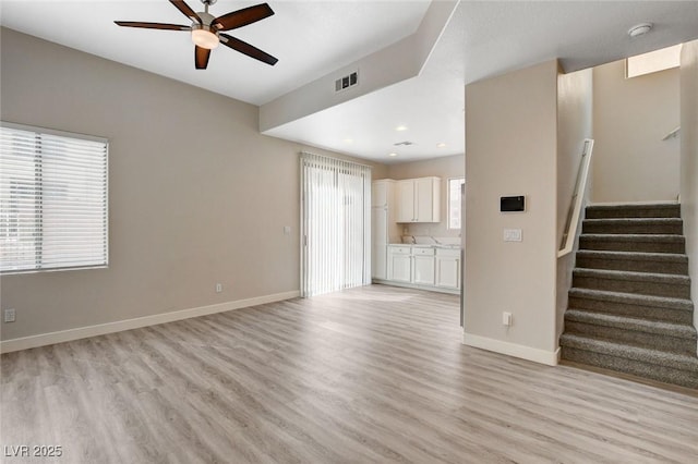 unfurnished living room featuring visible vents, light wood-style floors, baseboards, ceiling fan, and stairway