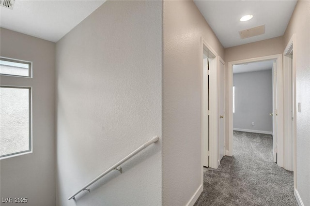 hall with carpet floors, visible vents, baseboards, and an upstairs landing