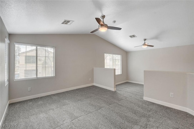 carpeted spare room with ceiling fan, vaulted ceiling, baseboards, and visible vents