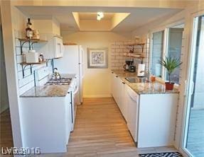 kitchen with white cabinets, white appliances, light countertops, light wood-type flooring, and a tray ceiling