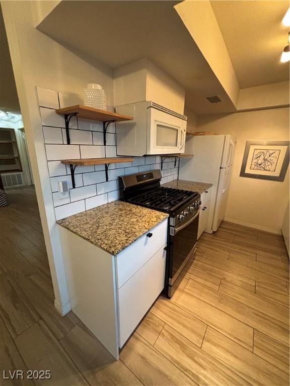 kitchen with light wood-style floors, gas range, white cabinetry, decorative backsplash, and white microwave