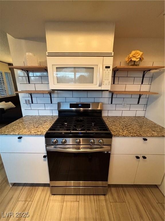 kitchen featuring open shelves, stainless steel range with gas stovetop, light wood-style flooring, decorative backsplash, and white microwave