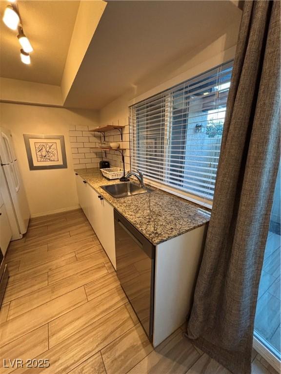 kitchen with light stone counters, a sink, light wood-style flooring, black dishwasher, and baseboards