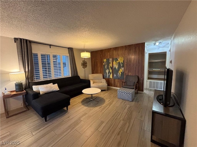 living room featuring baseboards, a textured ceiling, wood finished floors, and wooden walls