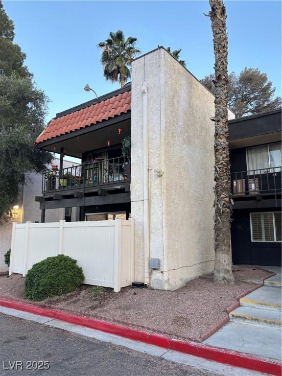view of property exterior featuring a tile roof, fence, a balcony, and stucco siding