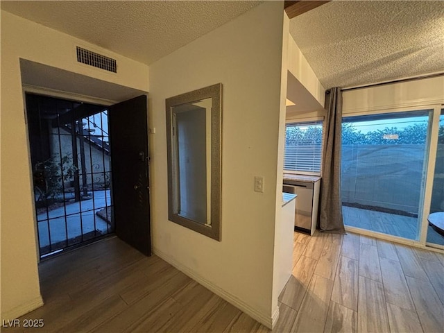 hall with a textured ceiling, wood finished floors, and visible vents