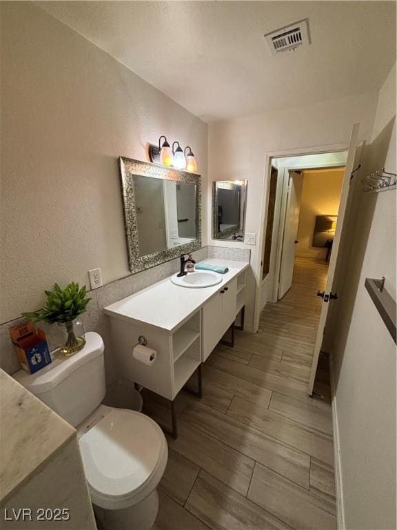 bathroom featuring wood finish floors, a textured wall, vanity, toilet, and visible vents