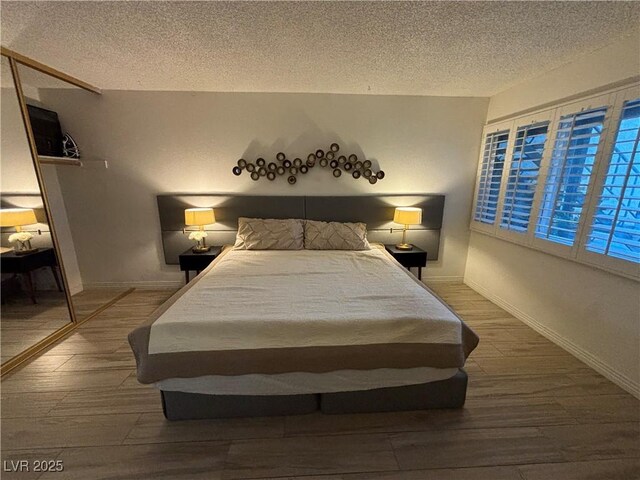 bedroom with baseboards, a textured ceiling, and wood finished floors