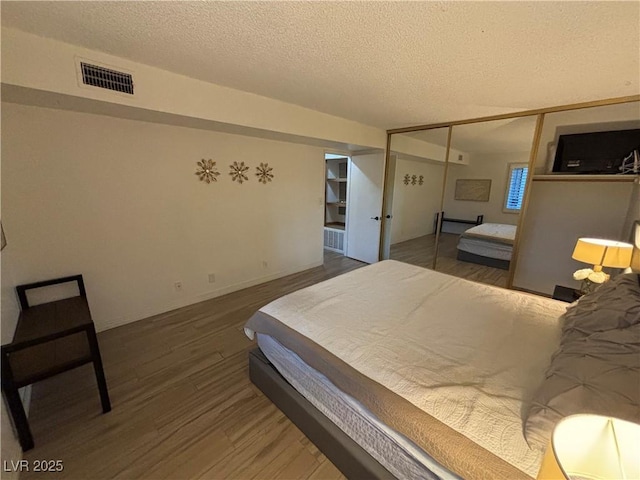 bedroom with visible vents, a textured ceiling, wood finished floors, and a closet