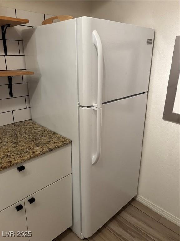 kitchen with backsplash, light stone counters, baseboards, freestanding refrigerator, and light wood-style floors