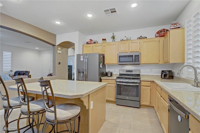 7013 Bisoni St, Las Vegas, NV 89149 - kitchen with stainless steel appliances, light brown cabinetry, a sink, a kitchen bar, and light stone countertops