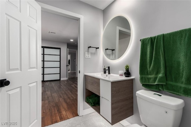 bathroom with vanity, toilet, baseboards, wood finished floors, and visible vents
