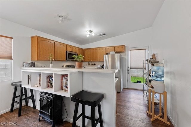 kitchen featuring appliances with stainless steel finishes, a kitchen breakfast bar, dark wood-style flooring, and visible vents