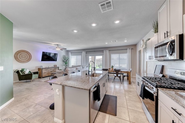 kitchen featuring visible vents, a center island with sink, light stone counters, a sink, and appliances with stainless steel finishes