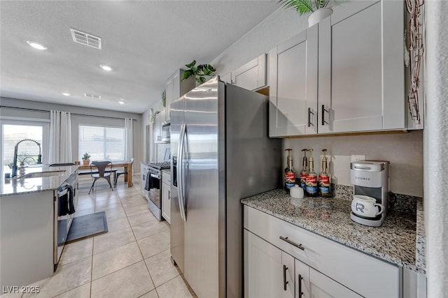 kitchen with visible vents, light stone countertops, a sink, light tile patterned floors, and stainless steel appliances
