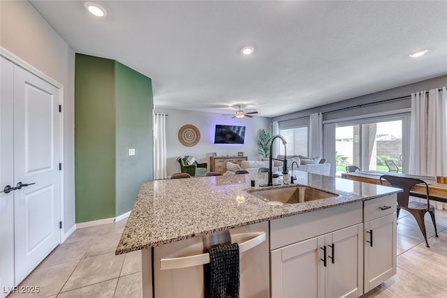 kitchen featuring light stone countertops, a sink, light tile patterned floors, open floor plan, and an island with sink