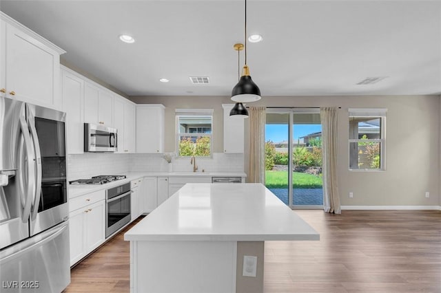 kitchen featuring visible vents, decorative backsplash, a kitchen island, a sink, and stainless steel appliances