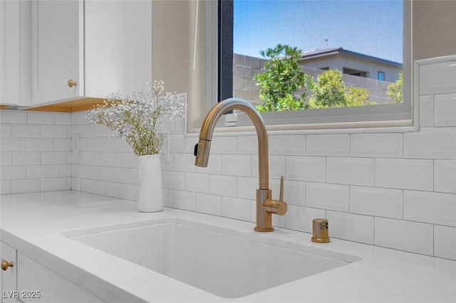 details featuring a sink, white cabinetry, tasteful backsplash, and light countertops