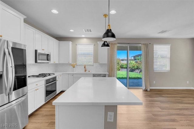 kitchen with appliances with stainless steel finishes, a sink, light countertops, backsplash, and a kitchen island