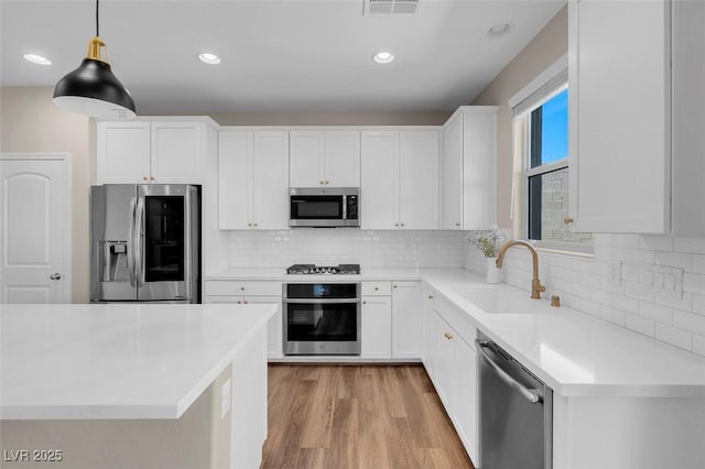kitchen featuring white cabinets, a sink, light wood-style flooring, backsplash, and stainless steel appliances
