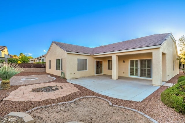 rear view of house with a patio, stucco siding, and a fire pit