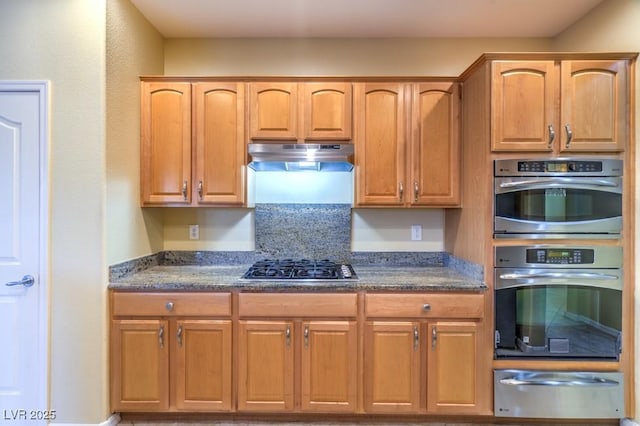 kitchen with dark stone counters, a warming drawer, under cabinet range hood, and stainless steel appliances