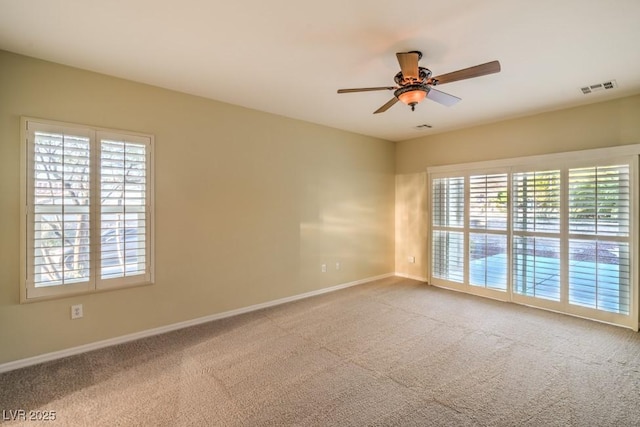 carpeted spare room featuring visible vents, baseboards, ceiling fan, and a wealth of natural light