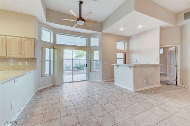 8052 Marbella Cir, Las Vegas, NV 89128 - kitchen with light brown cabinetry, ceiling fan, light countertops, a kitchen bar, and tasteful backsplash