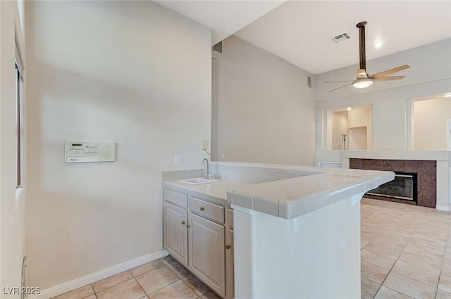 8052 Marbella Cir, Las Vegas, NV 89128 - kitchen with a peninsula, a sink, light tile patterned floors, a ceiling fan, and a fireplace