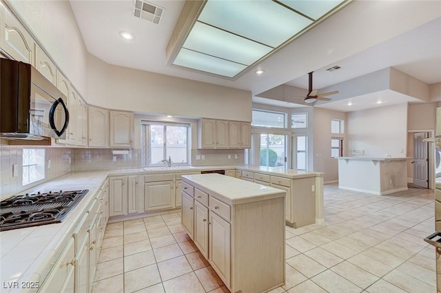 8052 Marbella Cir, Las Vegas, NV 89128 - kitchen with light tile patterned floors, stovetop with downdraft, decorative backsplash, a kitchen island, and recessed lighting