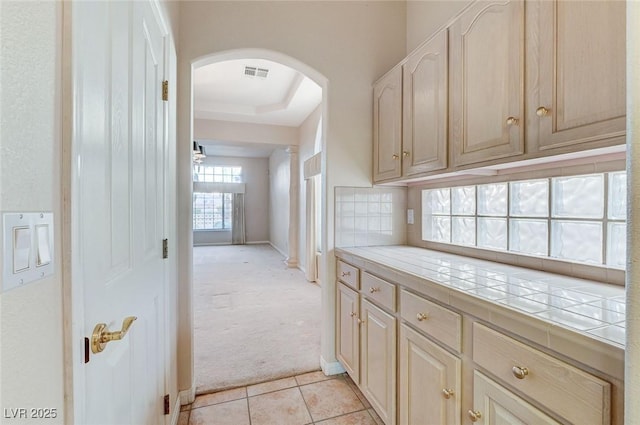 8052 Marbella Cir, Las Vegas, NV 89128 - kitchen featuring arched walkways, tile counters, light colored carpet, light tile patterned floors, and baseboards
