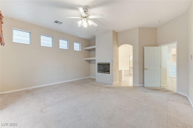 8052 Marbella Cir, Las Vegas, NV 89128 - unfurnished living room featuring arched walkways, light carpet, a ceiling fan, a tiled fireplace, and baseboards