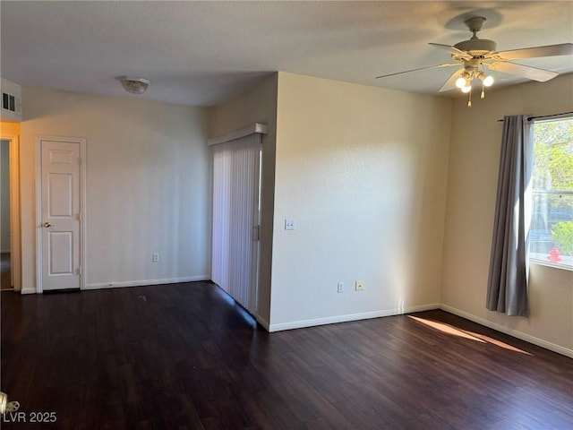 spare room featuring dark wood-style flooring, a ceiling fan, visible vents, and baseboards