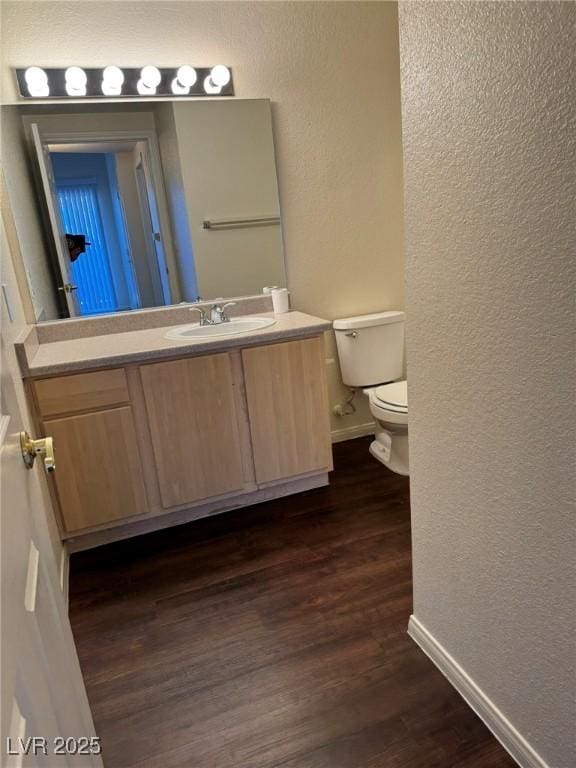 bathroom featuring wood finished floors, baseboards, vanity, toilet, and a textured wall