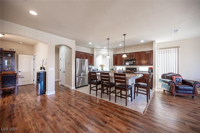 interior space featuring freestanding refrigerator, wood finished floors, black microwave, a breakfast bar, and arched walkways