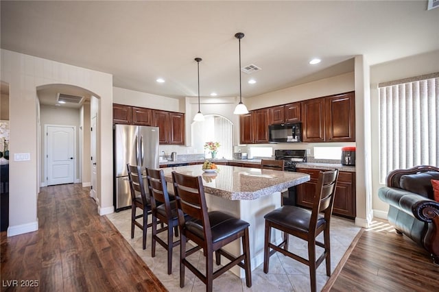 kitchen with a kitchen island, visible vents, black microwave, arched walkways, and freestanding refrigerator
