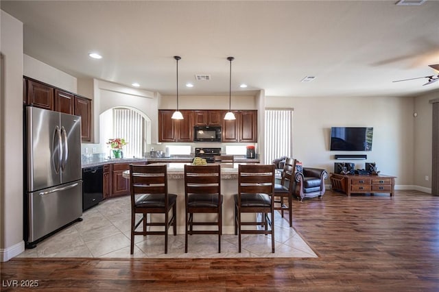 kitchen featuring a kitchen breakfast bar, open floor plan, light wood-type flooring, a kitchen island, and black appliances
