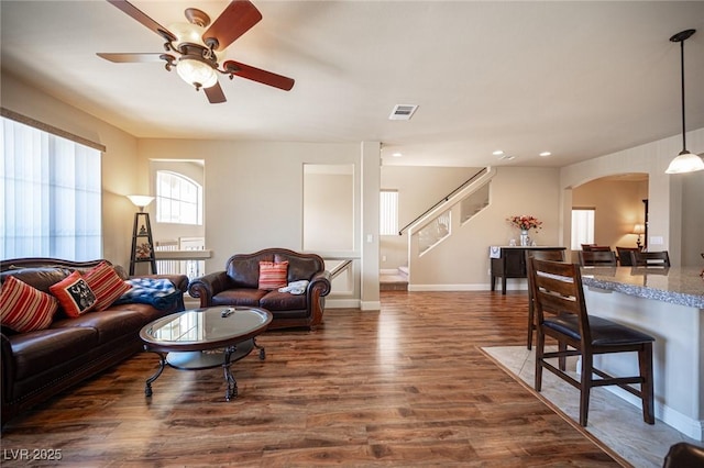 living room with visible vents, ceiling fan, stairway, arched walkways, and dark wood finished floors