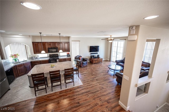kitchen featuring light stone counters, a sink, a center island, wood finished floors, and black appliances