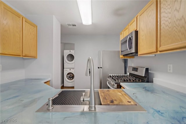 9932 Keephills St, Las Vegas, NV 89183 - kitchen featuring visible vents, light brown cabinetry, stacked washing maching and dryer, a sink, and stainless steel appliances