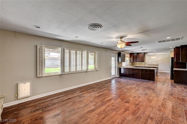 kitchen with dark brown cabinetry, visible vents, light countertops, a peninsula, and open floor plan
