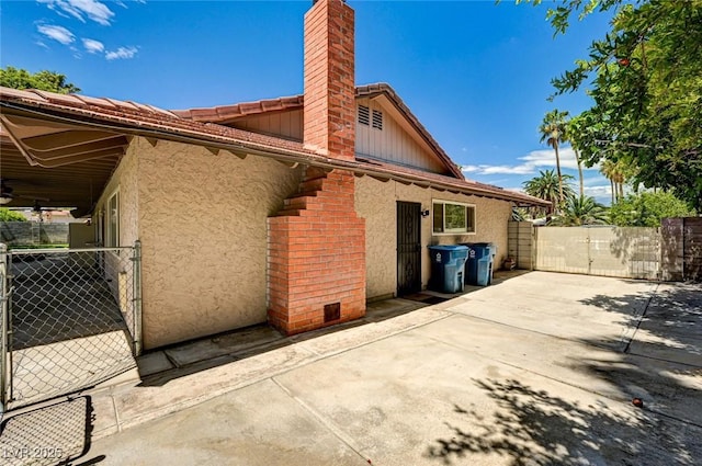 rear view of house with fence, stucco siding, a chimney, a gate, and a patio area