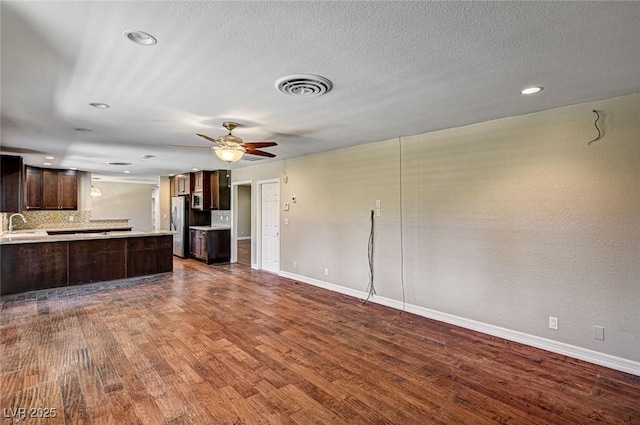 unfurnished living room with dark wood-style flooring, baseboards, visible vents, and ceiling fan