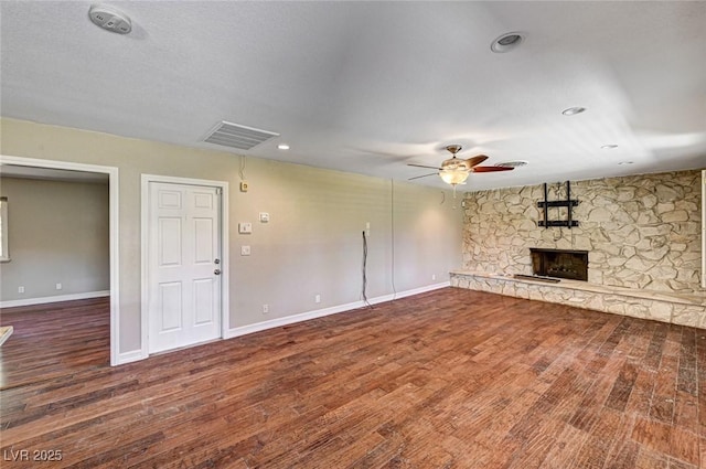 unfurnished living room with visible vents, wood finished floors, baseboards, a stone fireplace, and a ceiling fan