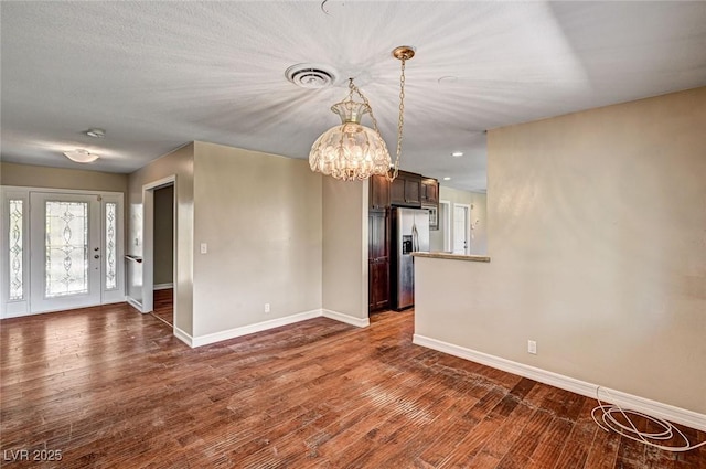 unfurnished living room featuring baseboards, dark wood-style flooring, a notable chandelier, and visible vents