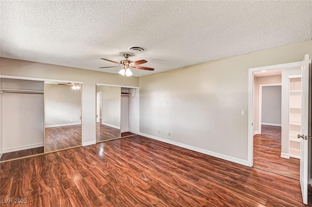 unfurnished bedroom with baseboards, a textured ceiling, multiple closets, and wood finished floors