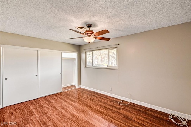 unfurnished bedroom with ceiling fan, a textured ceiling, baseboards, wood finished floors, and a closet
