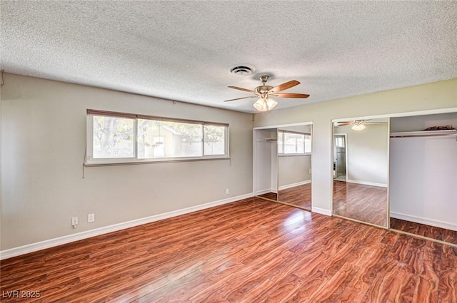unfurnished bedroom featuring visible vents, wood finished floors, two closets, baseboards, and a textured ceiling